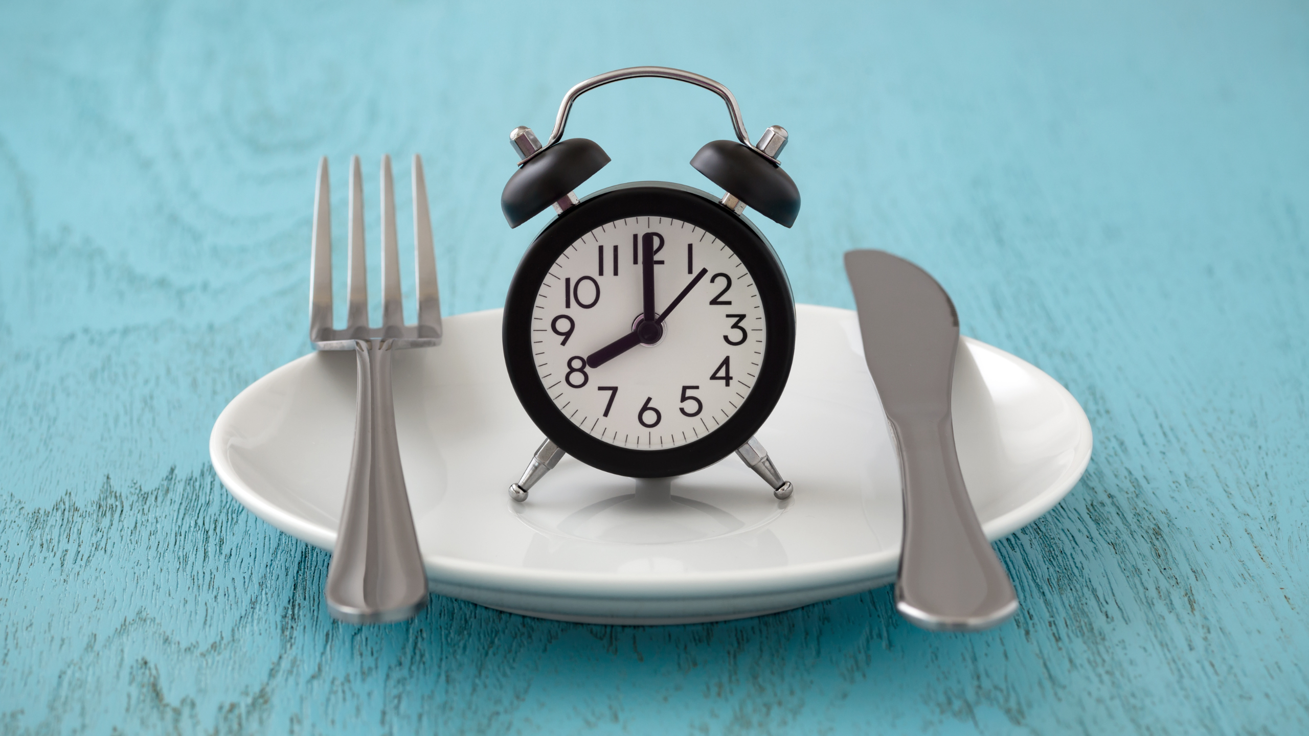 Image of a plate with a fork, knife, and alarm clock but no food on it representing fasting.